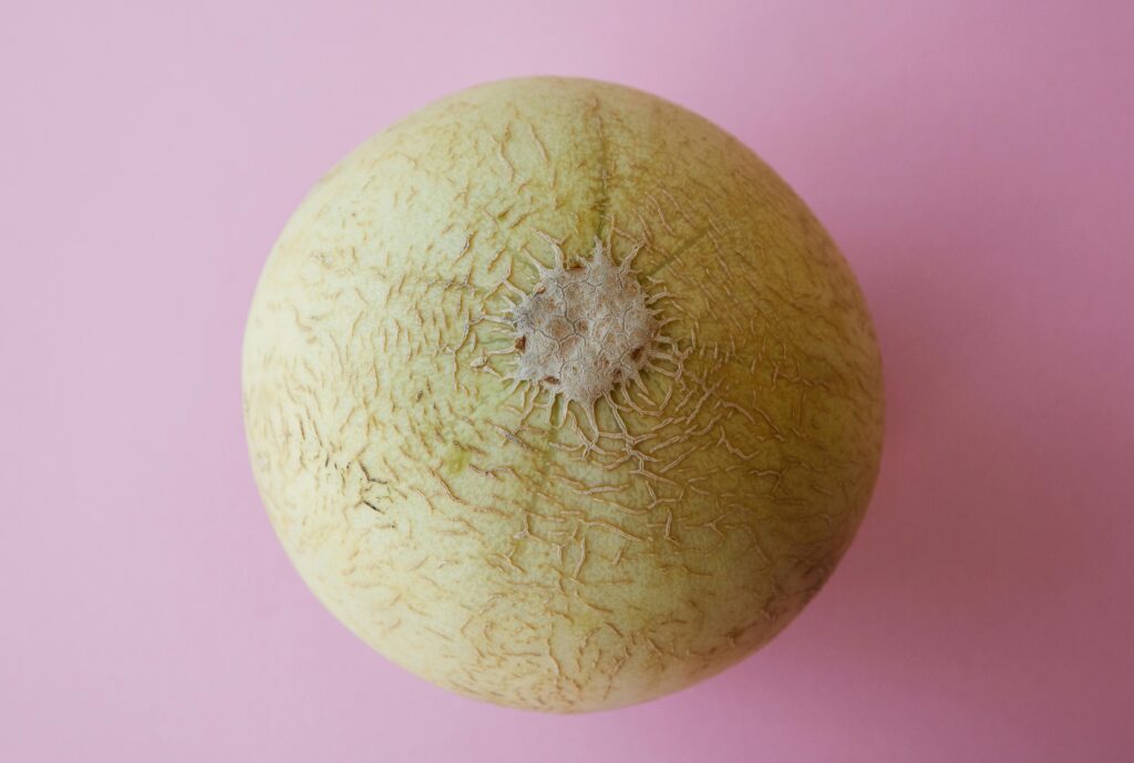 Healthy and ripe melon on pink surface, showcasing natural texture and vibrant color.